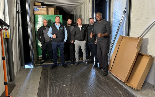 Volunteers giving a thumbs-up at a loaded container of donated IT equipment
